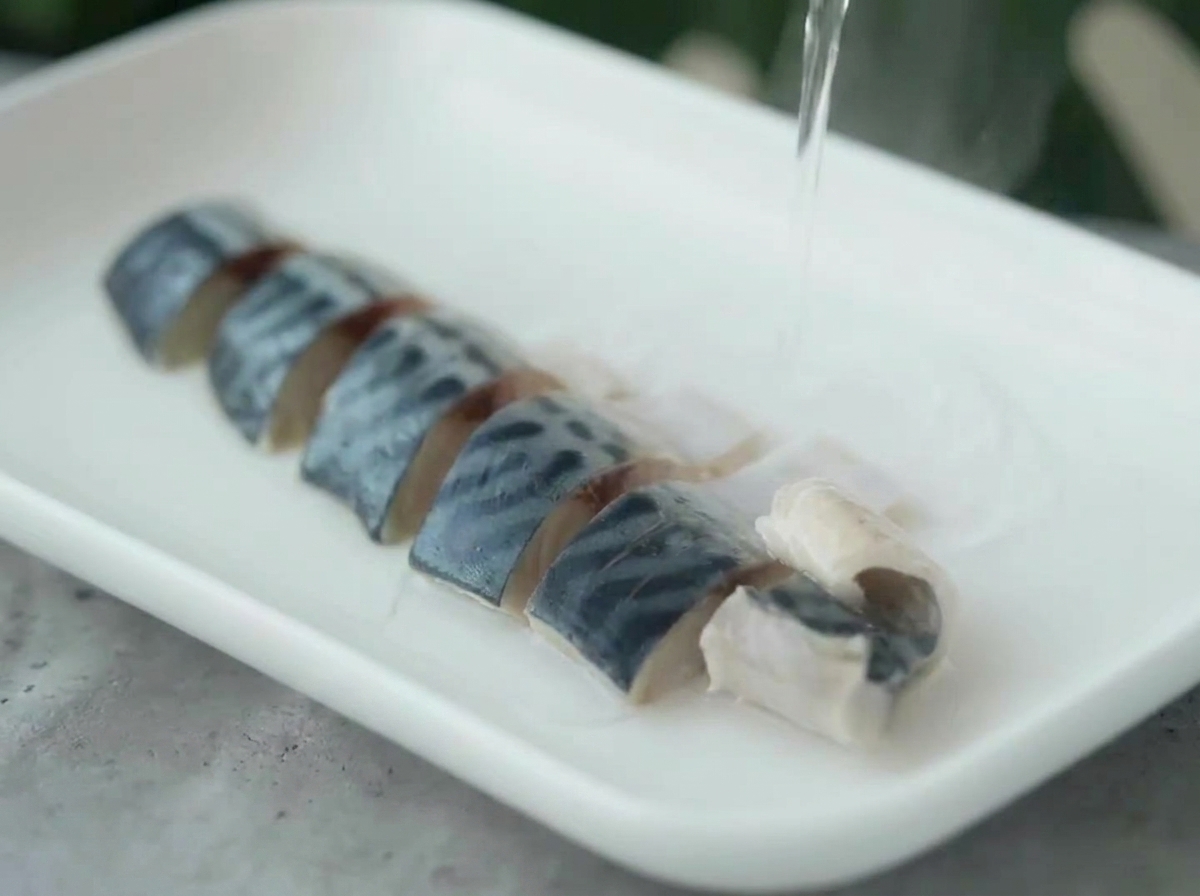 皿に並べた鯖の切り身に、ケトルから熱湯をかけている様子。