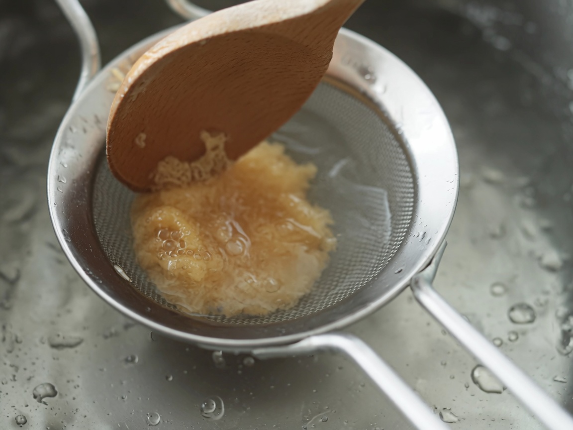 鍋の上でザルと木べらを使って味噌を丁寧に溶かしている様子。