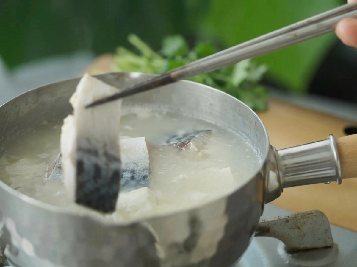 菜箸で霜降りした鯖を鍋に加えている様子。