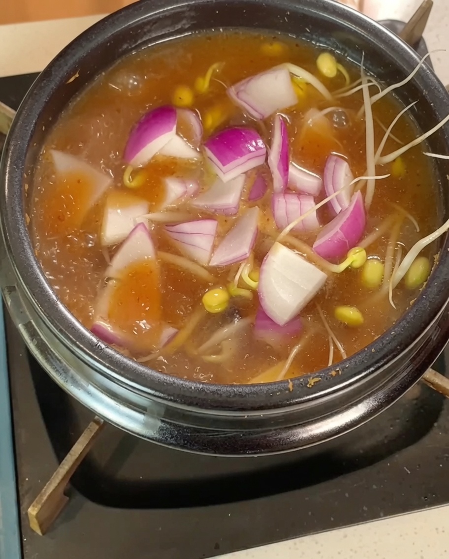 煮立っている鍋にもやし、玉ねぎ、豆腐を加えている様子。