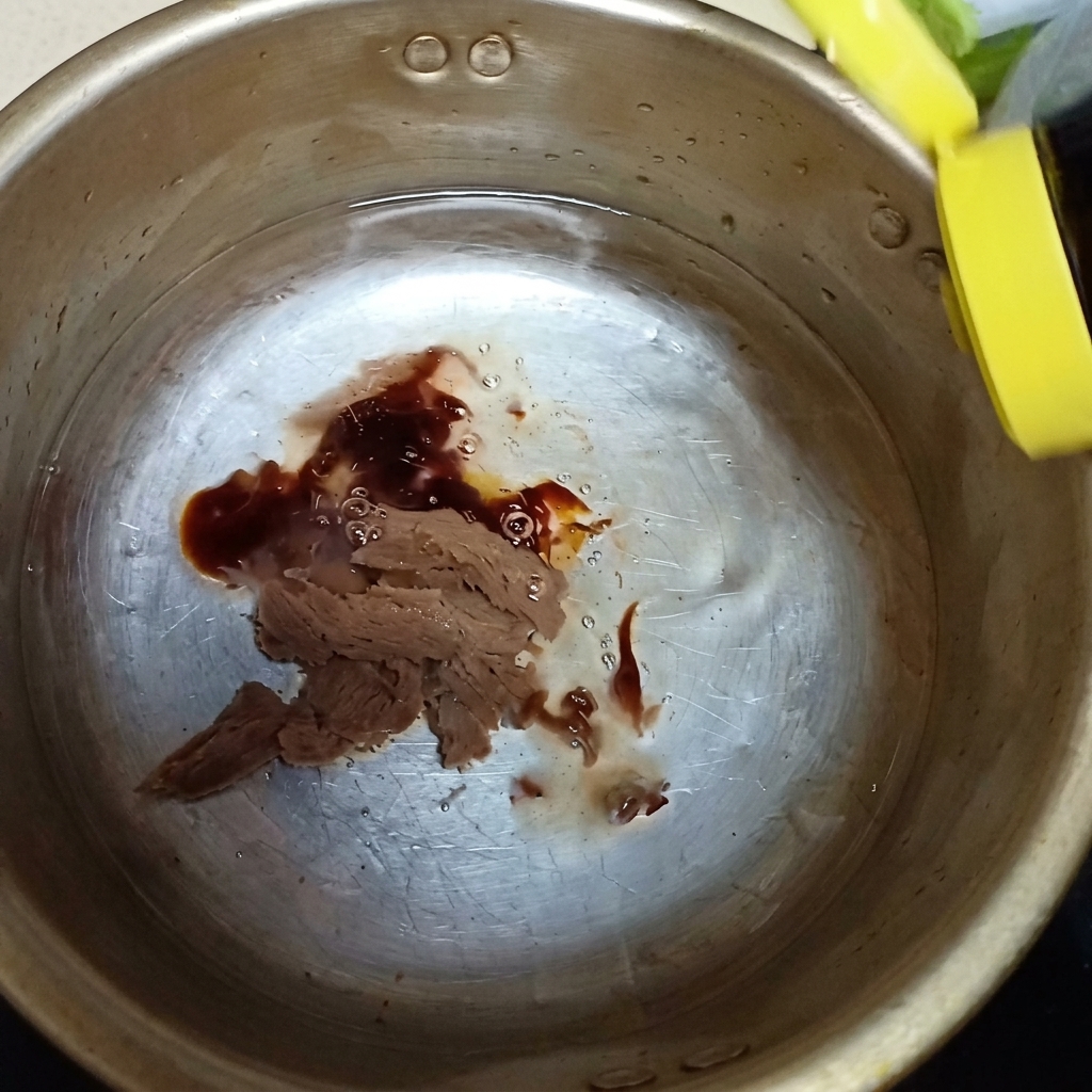 鍋の中の味噌の上からオイスターソースと少量のナンプラーを注ぐ様子。