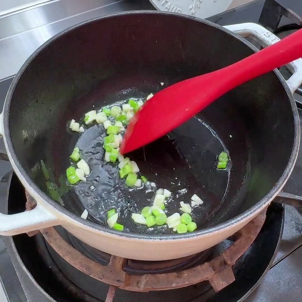 鍋で刻んだネギとにんにくを少量の油で炒めている様子。