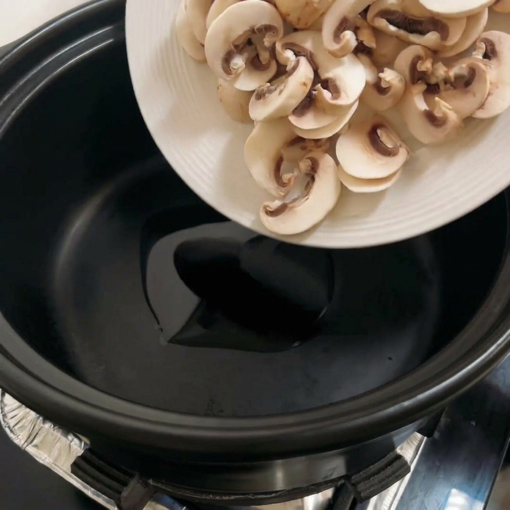 黒い鍋の中で、スライスされたポートベローキノコがキツネ色に炒められている様子。