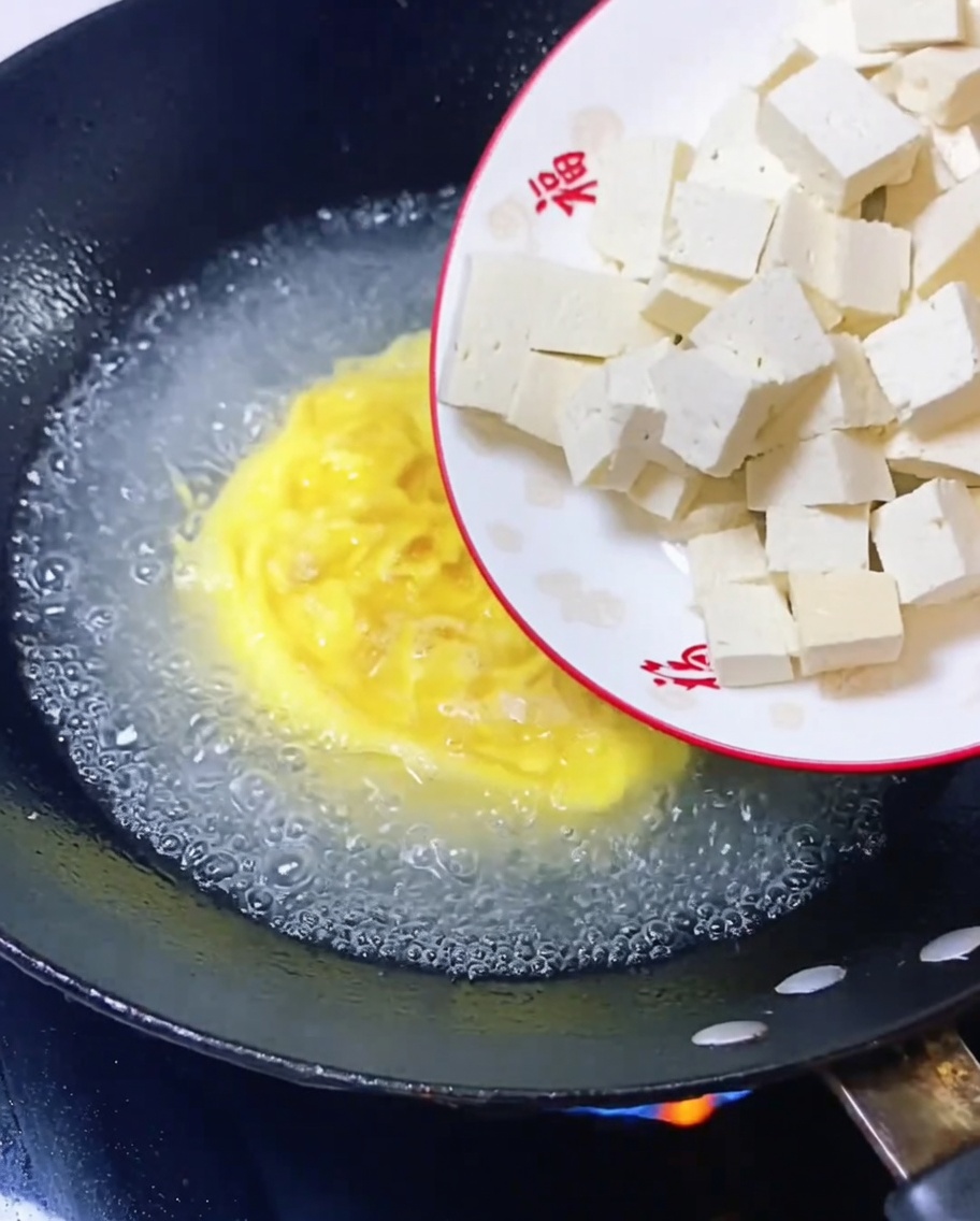 煮立っている卵スープに豆腐の角切りを入れている様子。