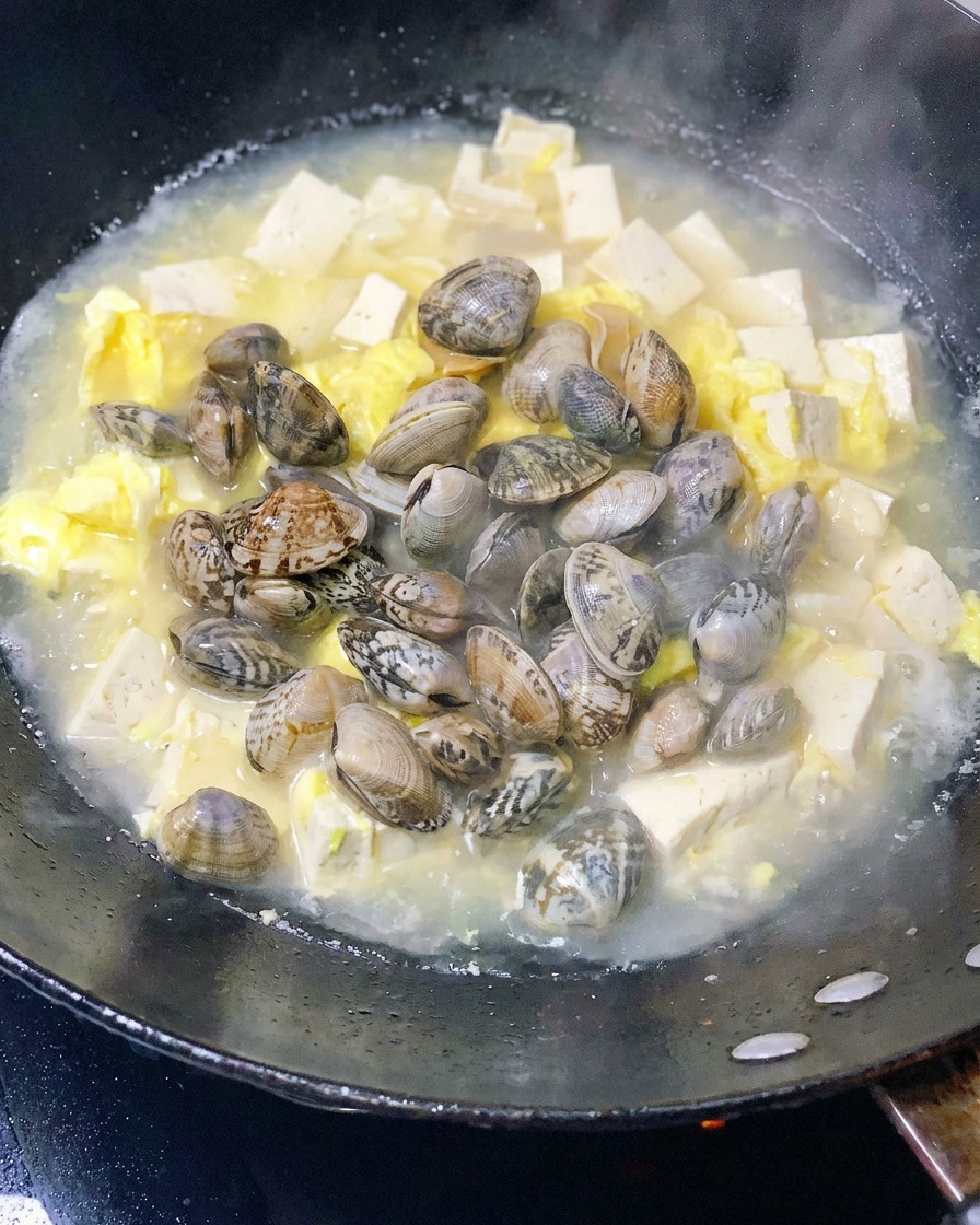 豆腐と卵のスープにアサリを加えている様子。