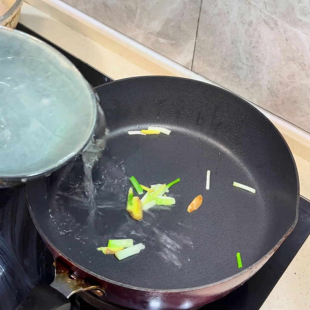 炒めた生姜とねぎの入ったフライパンに熱湯が注がれている様子。