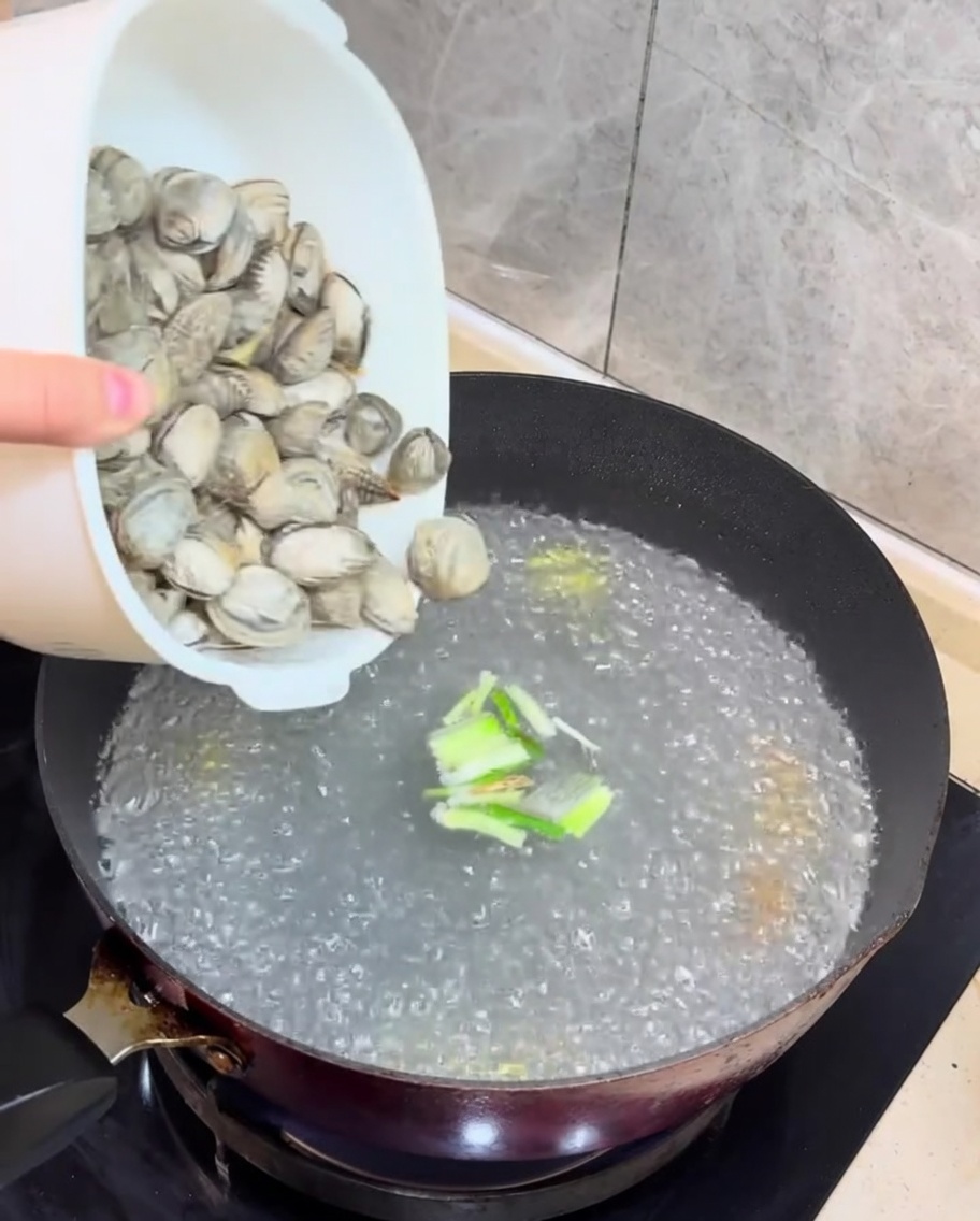 沸騰したスープに新鮮なあさりと角切りにした豆腐が加えられている様子。
