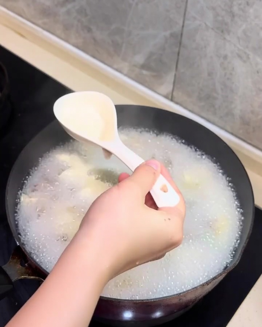 あさりと豆腐のスープの表面に浮かんだ白いアクをスプーンですくい取っている様子。
