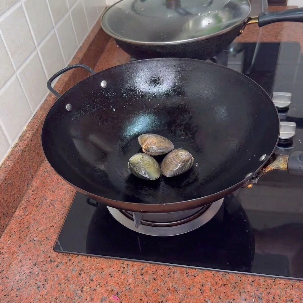 中華鍋の中で蒸されている3つのアサリ。
