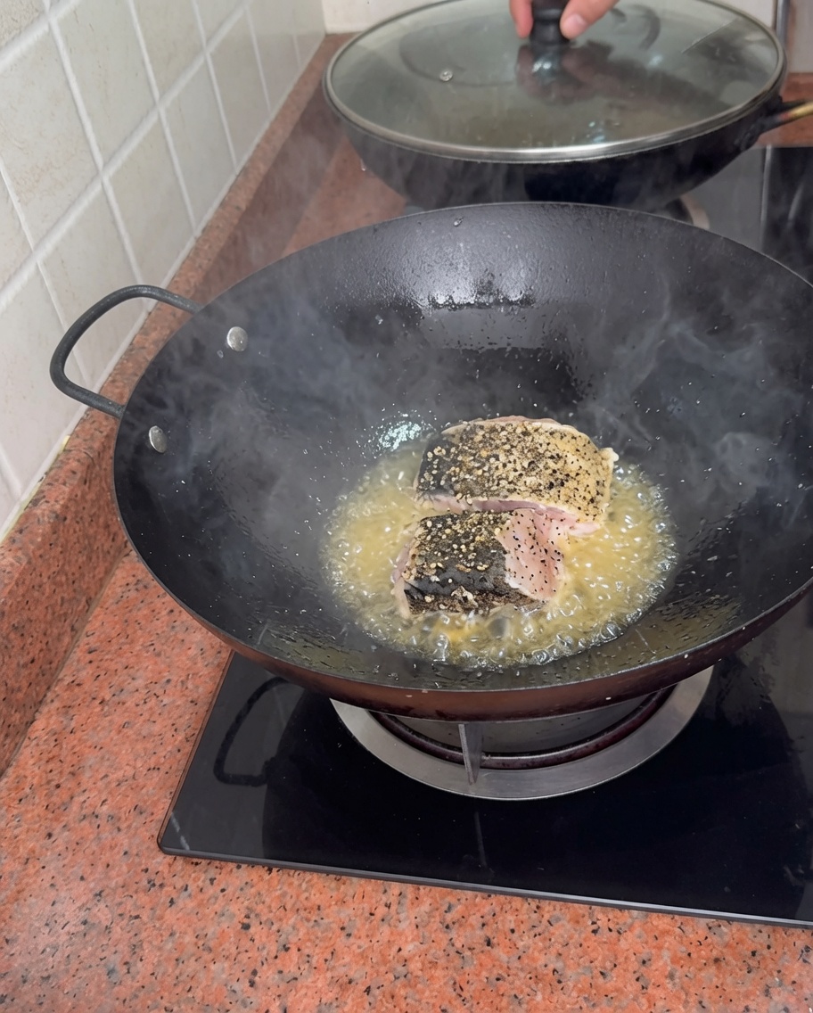 中華鍋の油で魚の切り身が焼かれている様子。