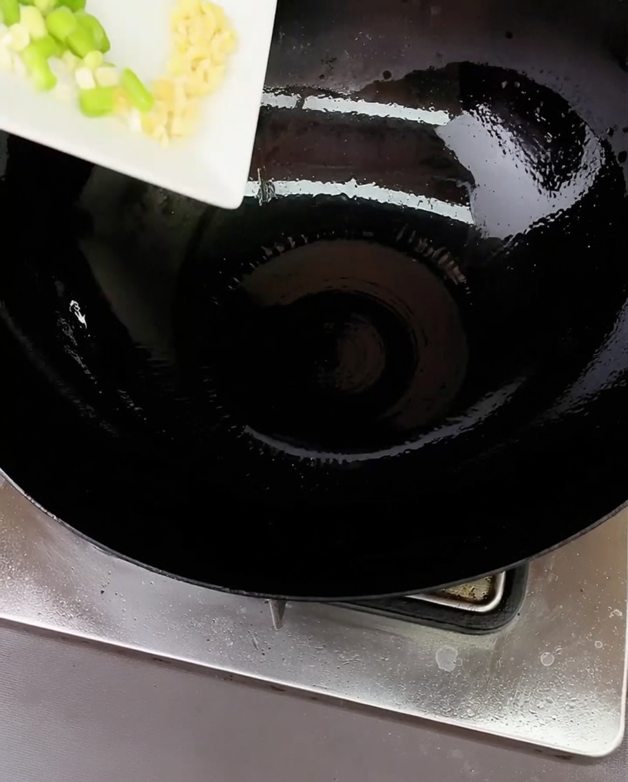 中華鍋で刻んだねぎとにんにくを油で炒めている様子。