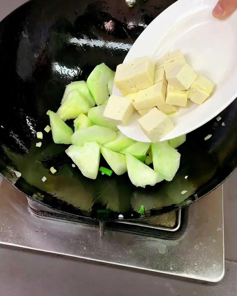 炒めたヘチマに豆腐とあさりを加えている様子。