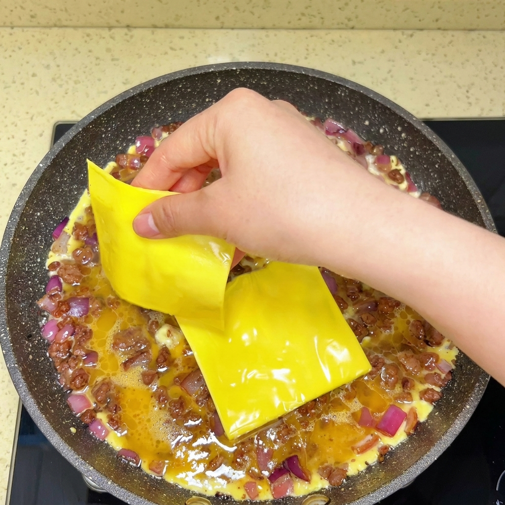調理中の卵と牛肉の上にスライスチーズがのせられている様子。