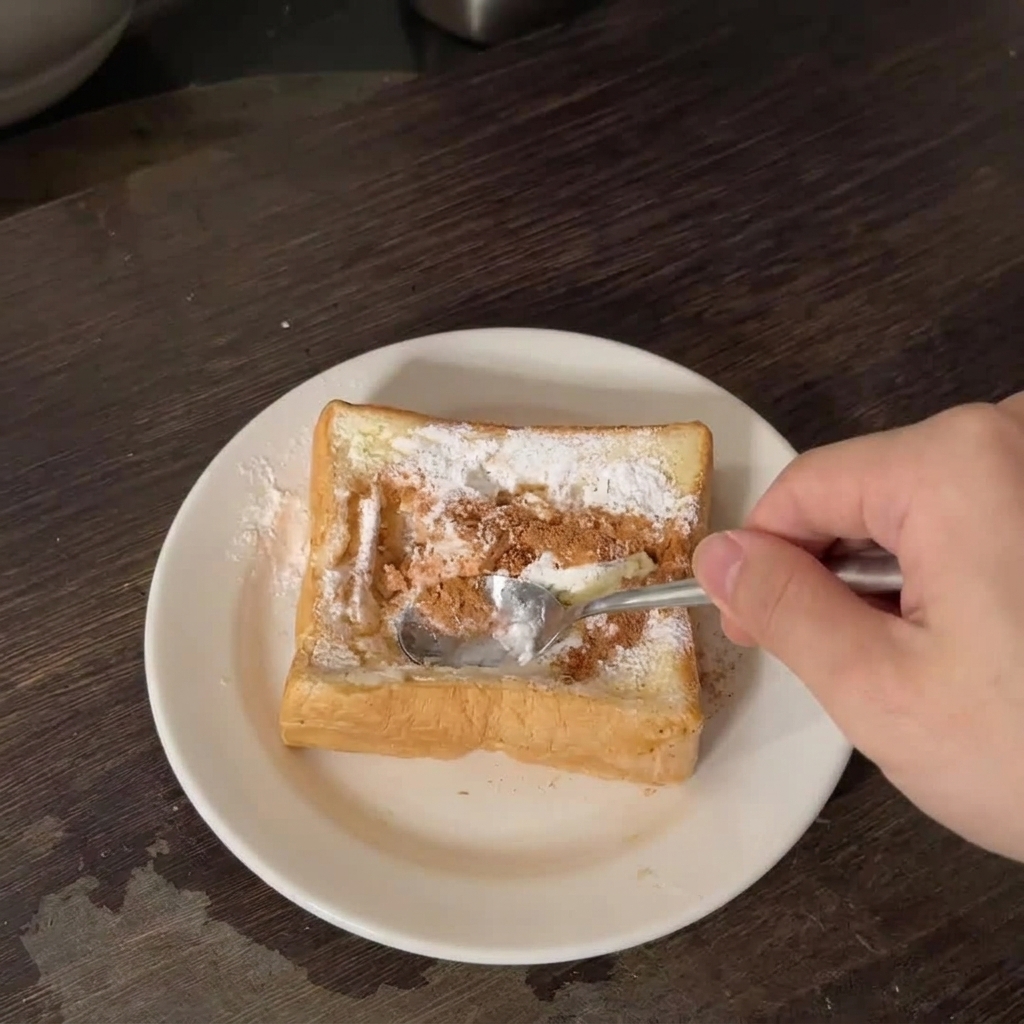 白いお皿の上で、厚切り食パンの中央を金属製のスプーンの背で押し込んでへこませている様子。