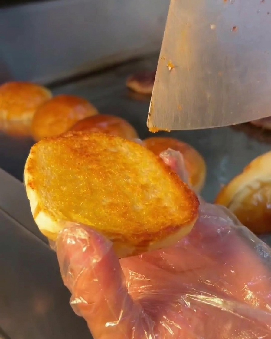 金属のスプーンで、焼いたバーガーバンズの内側に白いクリーミーなソースを塗っている様子。