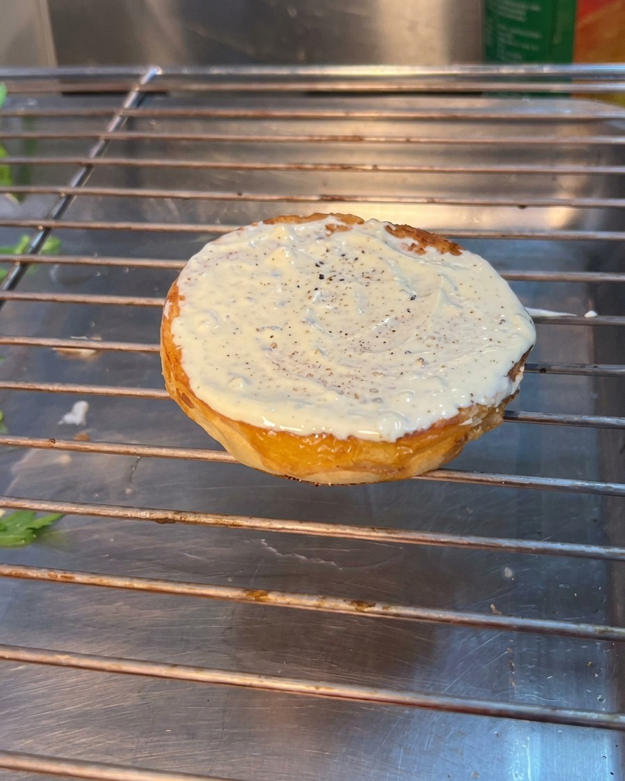 下のバンズの上にルッコラ、トマト、ピクルスが順番に重ねられているバーガーの組み立てシーン。