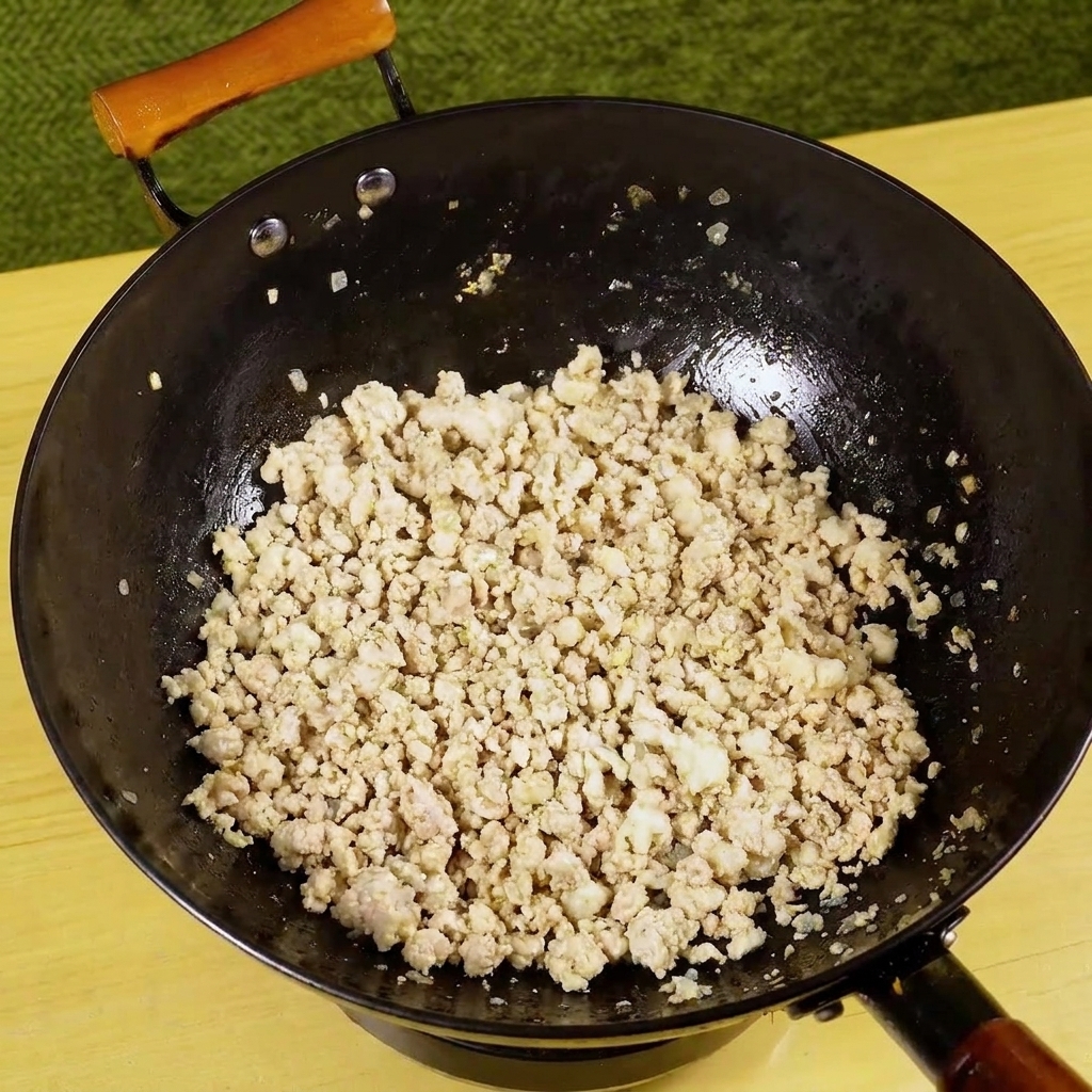 炒めたひき肉のフライパンに、刻んだ青唐辛子が加えられる様子。
