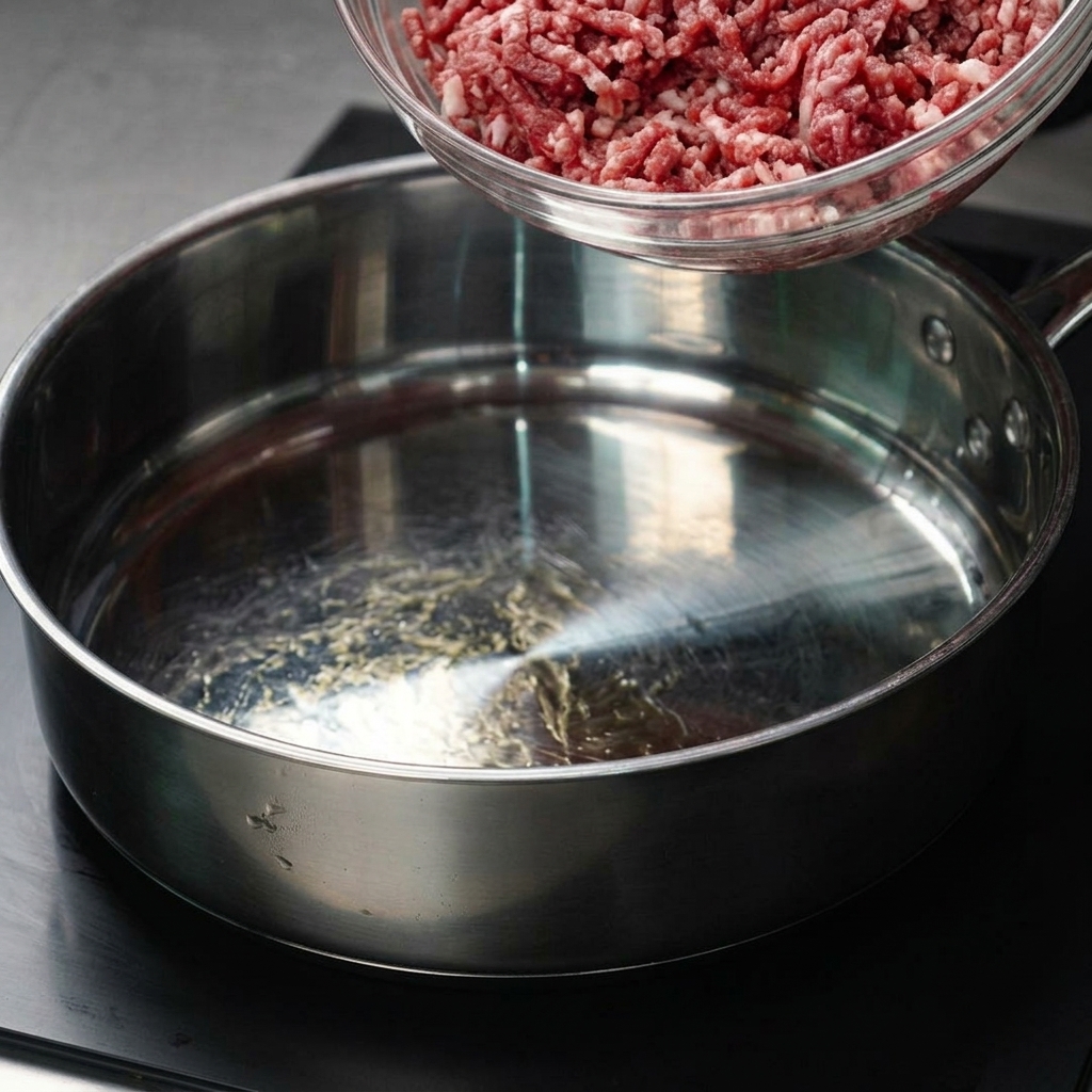 ガラスボウルから熱いフライパンへ牛ひき肉を移している様子。