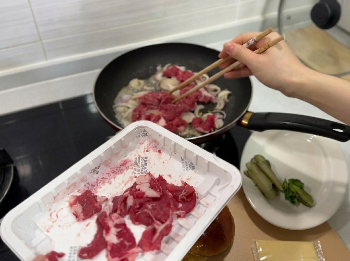 炒めた玉ねぎが入ったフライパンに加えられる生の薄切り牛肉。