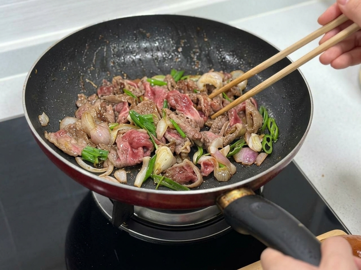 牛肉、玉ねぎ、ピーマンが一緒に炒められている様子。