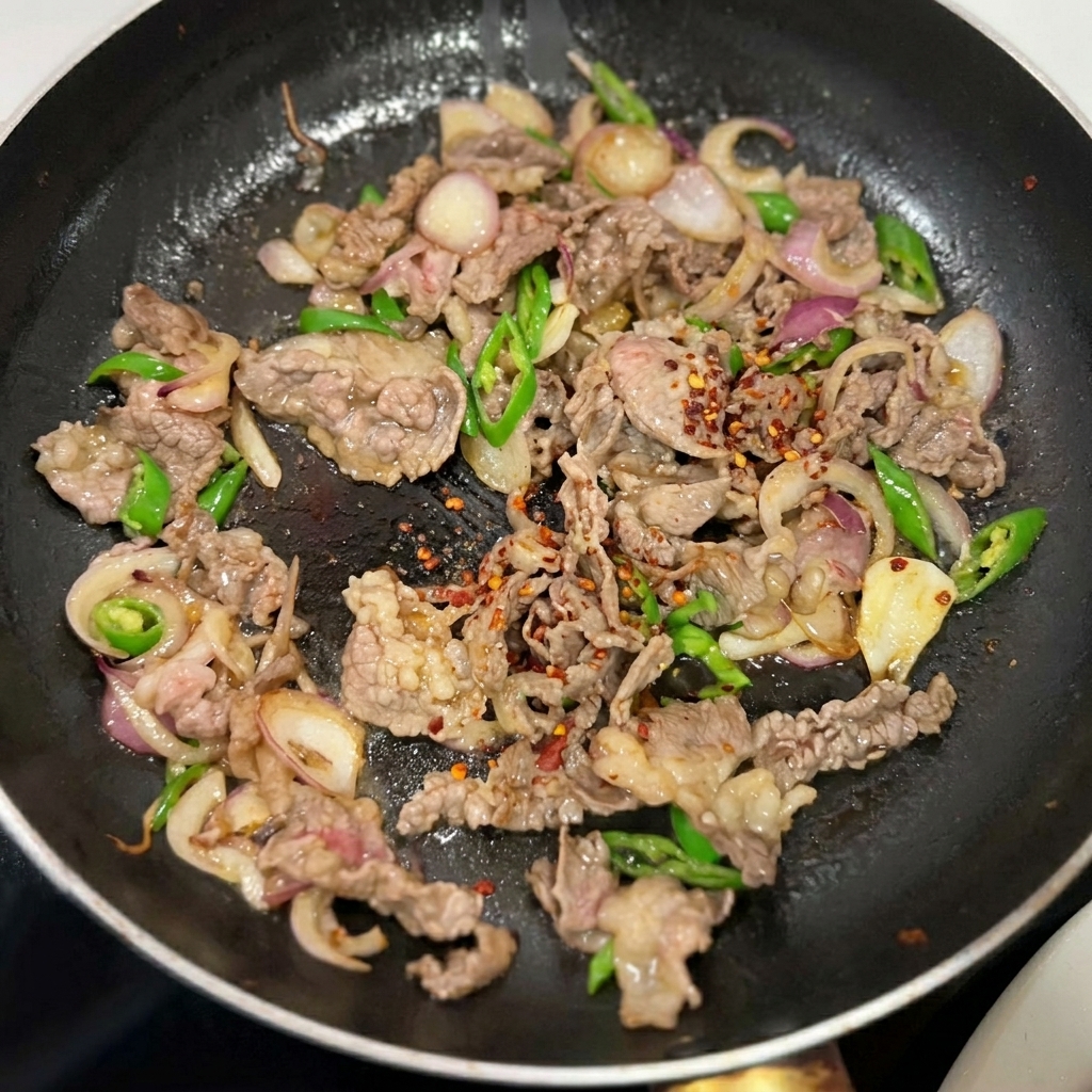 フライパンの中で牛肉や野菜に調味料が振りかけられている様子。