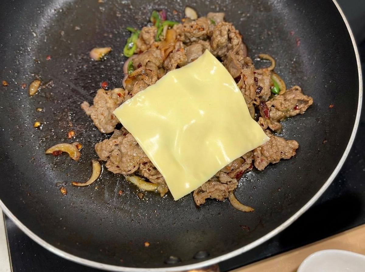 炒めた牛肉の上にのせられ、余熱で溶け始めているスライスチーズ。