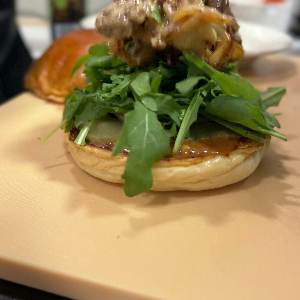 ルッコラの上に、チーズがとろけた牛肉の炒め物が積み重ねられている様子。