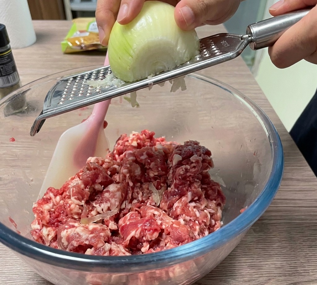 手持ちのおろし器でボウルの中の肉に玉ねぎをすりおろしている様子。