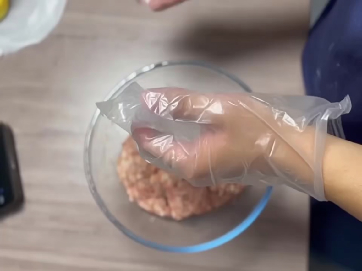 手袋をした手で肉をしっかりとした滑らかなボール状に成形している様子。