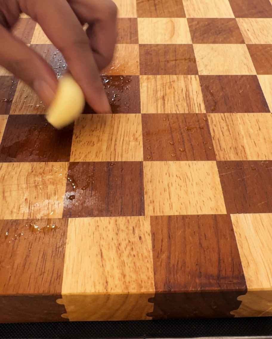木のまな板の上で大きな包丁を使って細かく刻まれているにんにく。