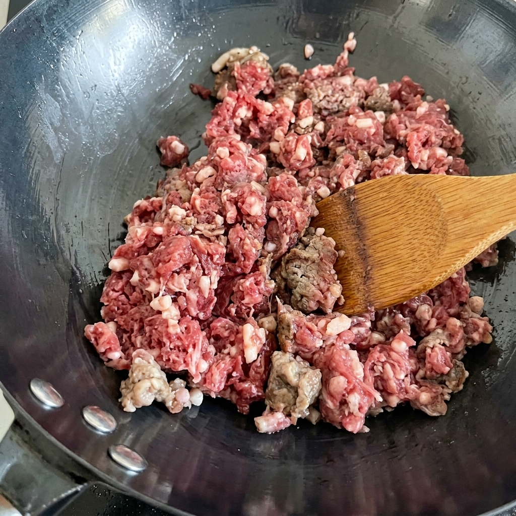 熱した中華鍋で、赤身から茶色に変わるまで炒められている牛ひき肉。