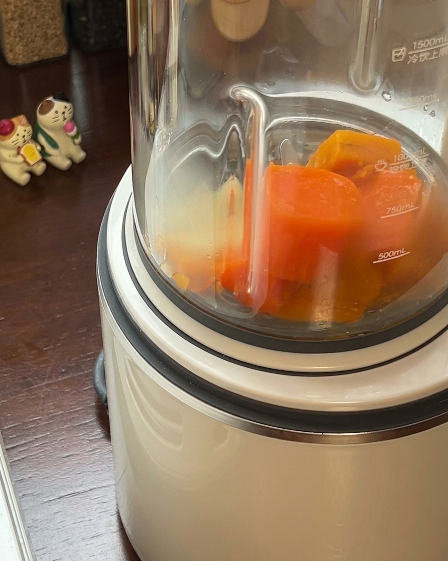 加熱したかぼちゃとにんじんを、高速ブレンダーの容器に注ぎ入れている様子。