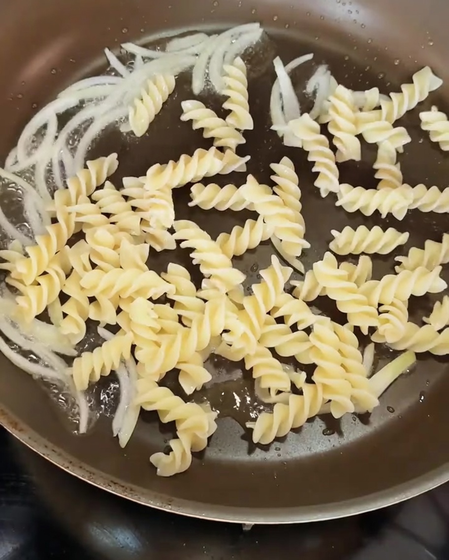 炒めた玉ねぎの入ったフライパンの中に、茹で上がった螺旋状のパスタを投入している様子。