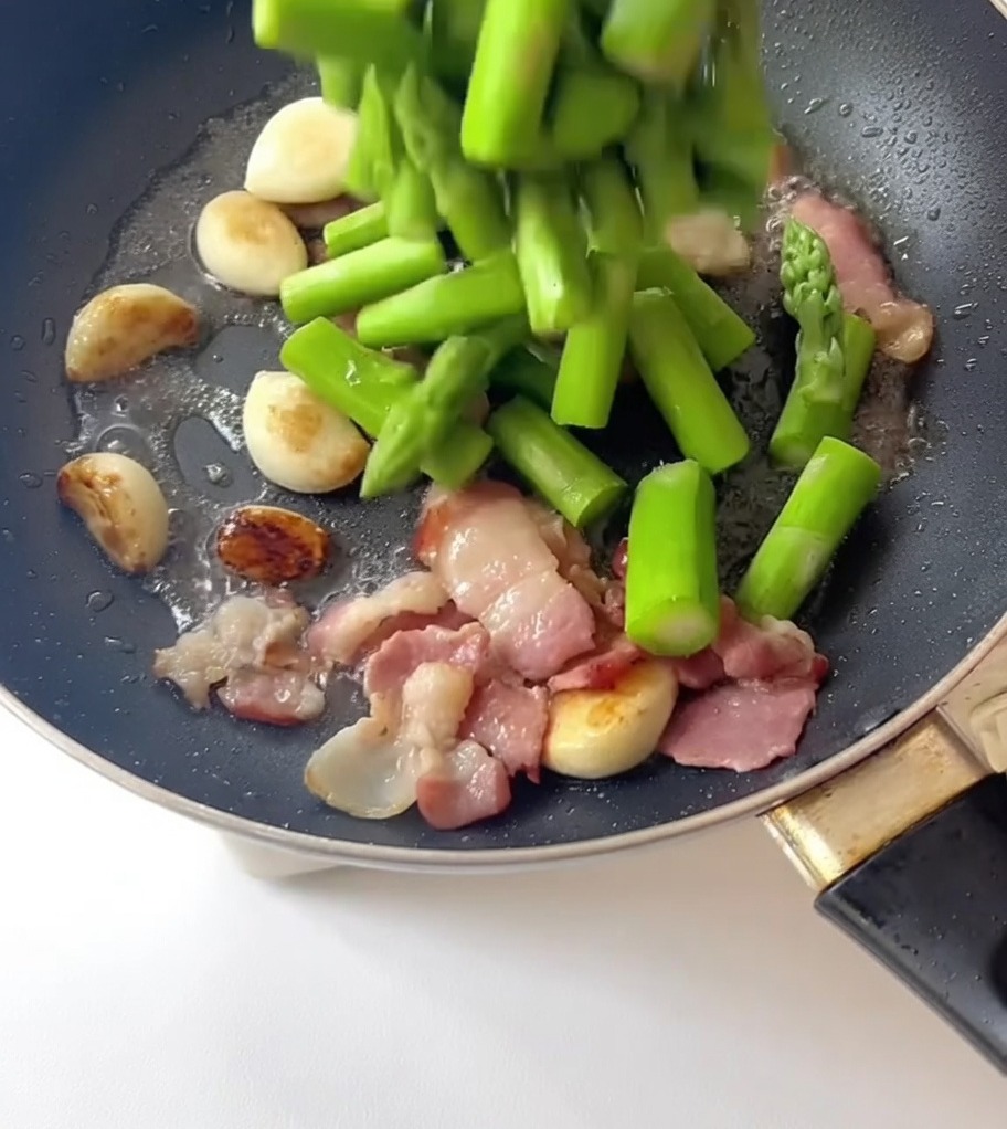 下茹でしたアスパラガスをフライパンに加える様子。