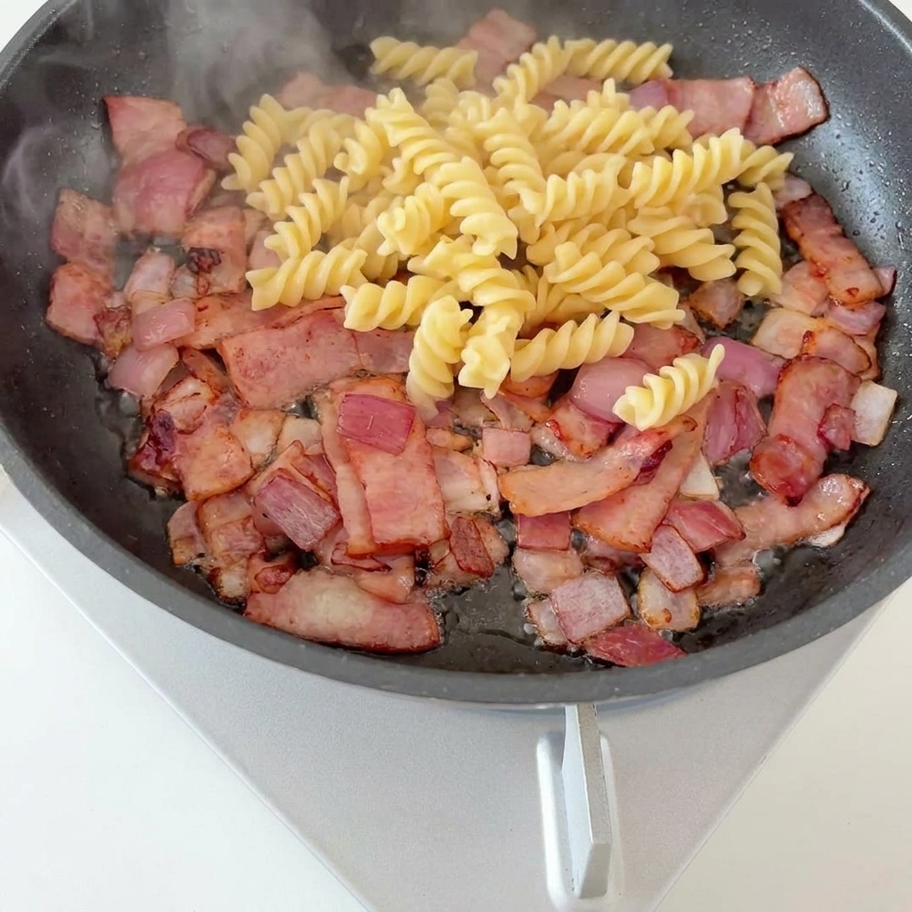 茹で上がったパスタとアスパラをフライパンに入れる様子。