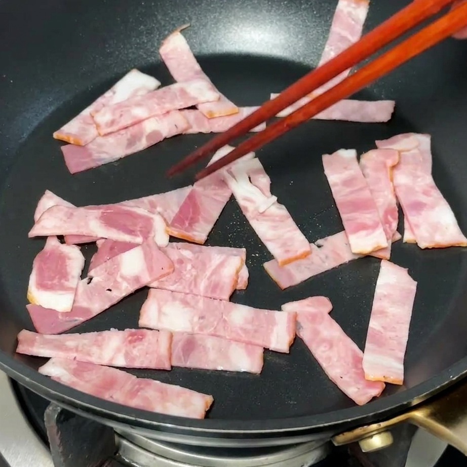 熱したフライパンでベーコンが色づき、脂が溶け出している様子。