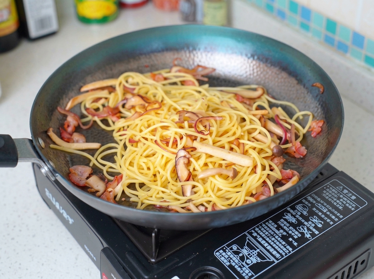 パスタと具材が入ったフライパンに牛乳を注いでいる様子。
