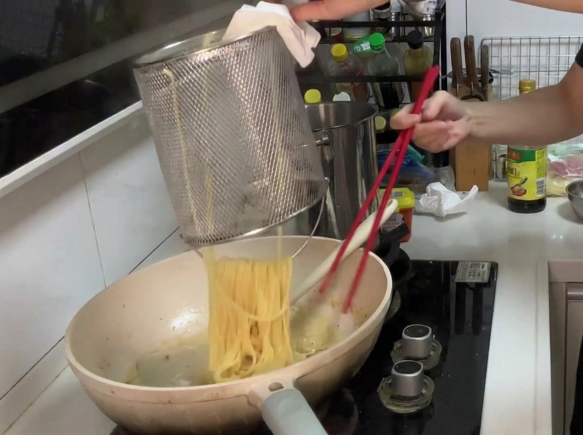 茹で上がったパスタをクリームソースに入れて絡めている様子。