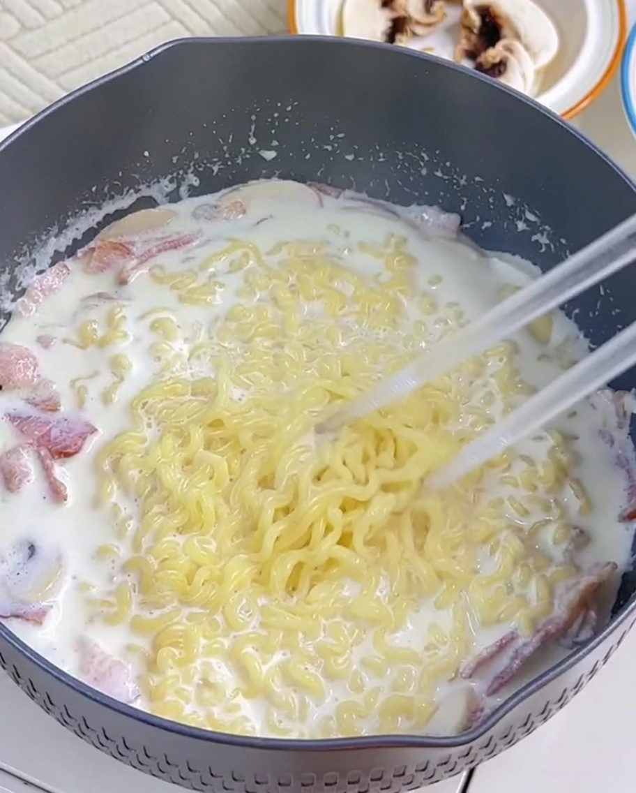 茹でたラーメン麺をクリーミーなソースの中に箸で絡めている様子。