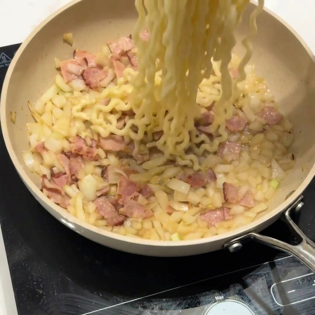 ベーコンと玉ねぎが入ったフライパンにカールパスタを加えている様子。