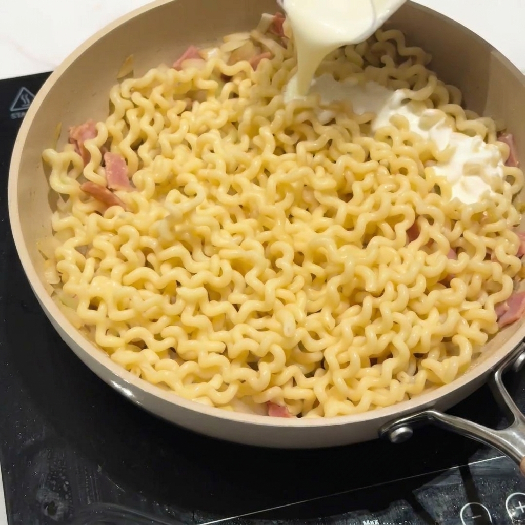 フライパンのパスタに低脂肪乳を注ぎ、ソースを作っている様子。