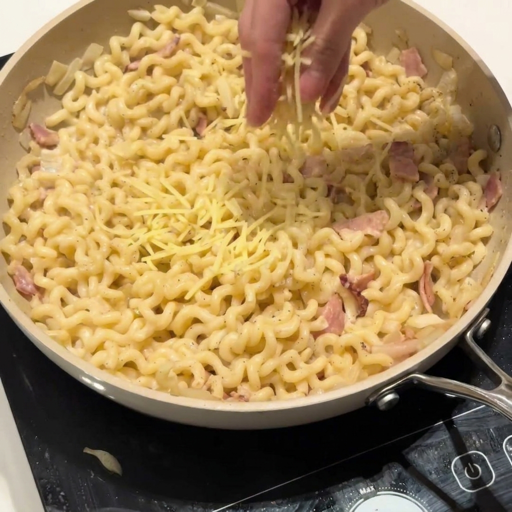 クリーミーなカールパスタの入ったフライパンの上に、たっぷりの粉チーズを振りかけている様子。
