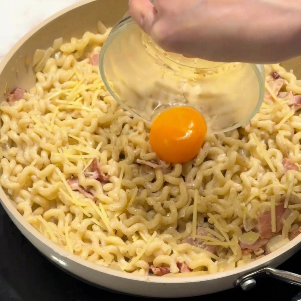 フライパンの中のクリーミーなパスタの中央に卵黄を落としている様子。