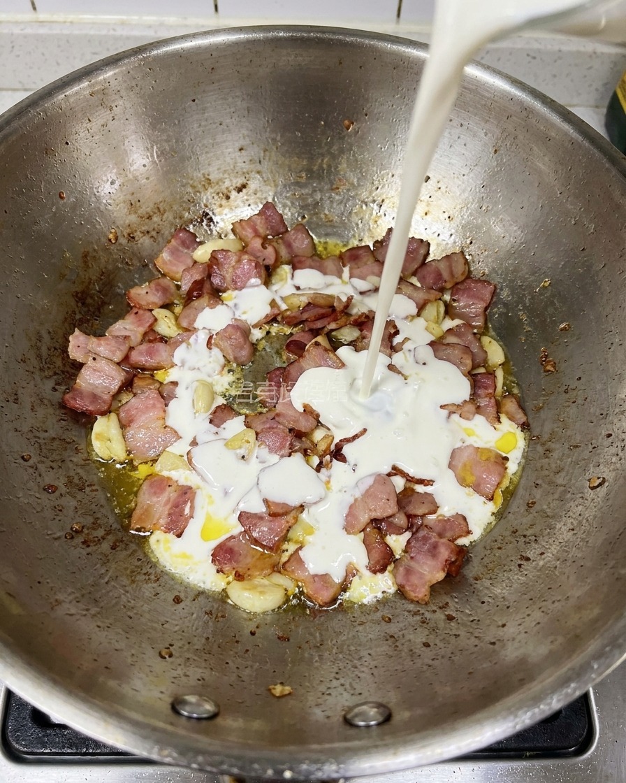 炒めたベーコンとにんにくが入ったフライパンに生クリームを注いでいる様子