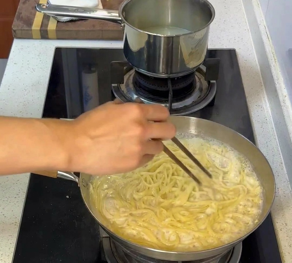トングを使ってクリームソースとパスタをしっかり絡める様子。