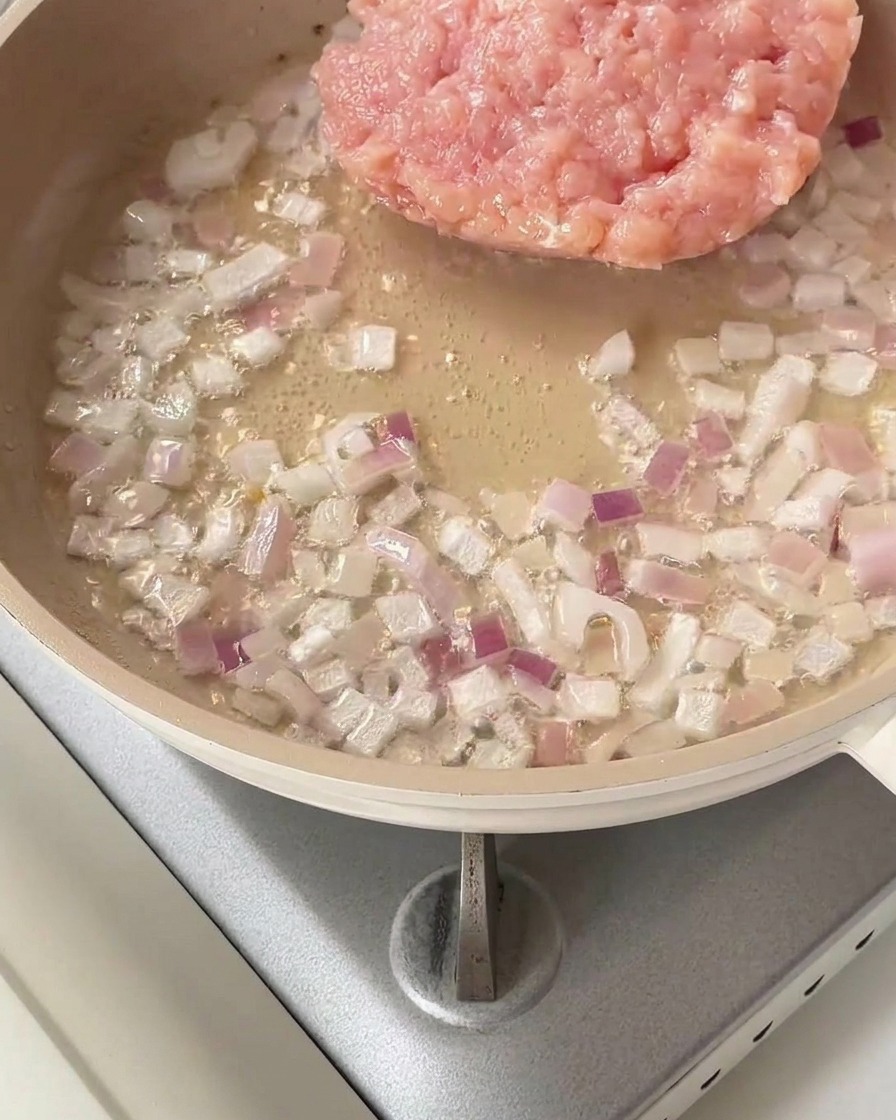 炒めた紫玉ねぎの入ったフライパンに生のみじん切り鶏肉を加えた様子