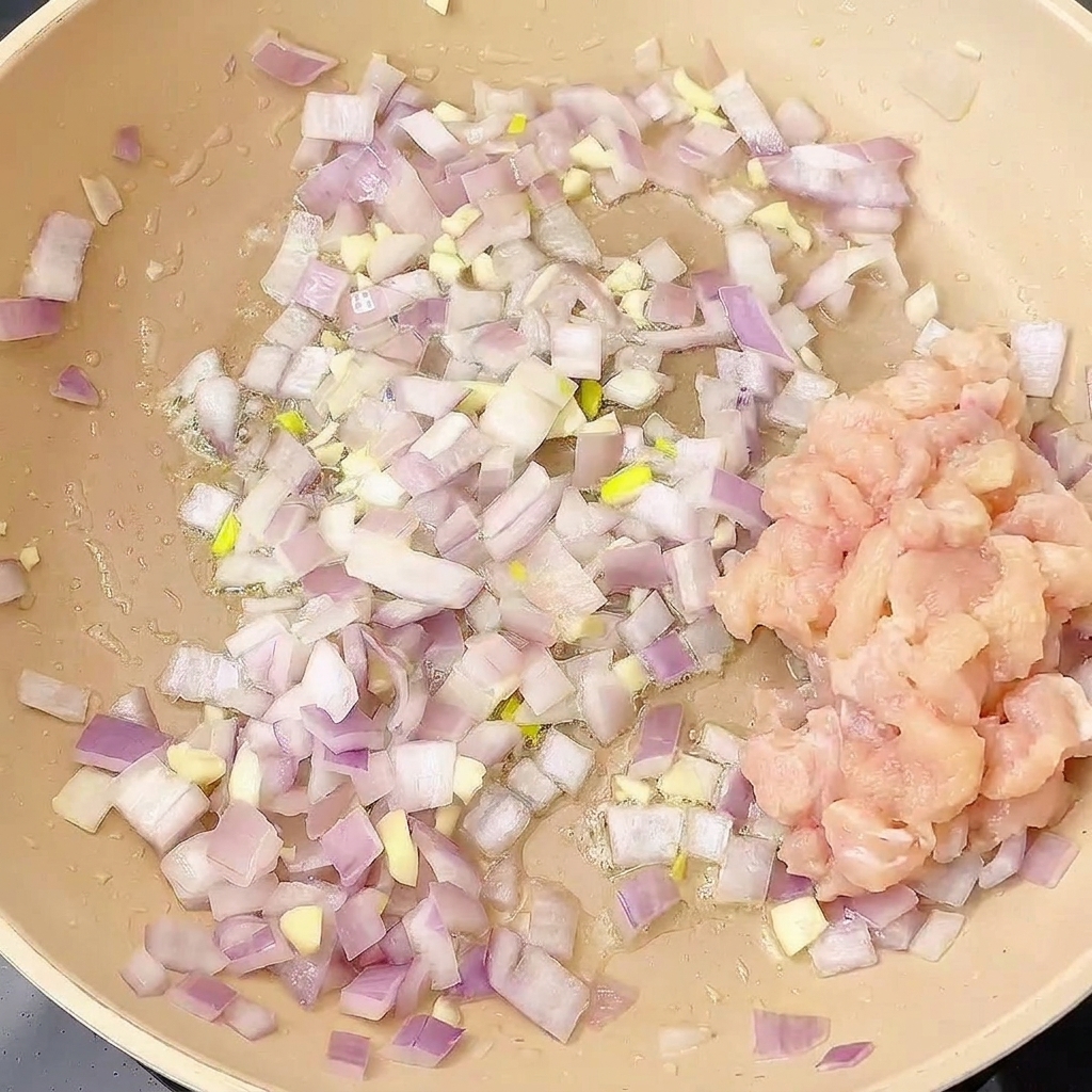 炒めた香味野菜のフライパンに鶏肉を加えている様子