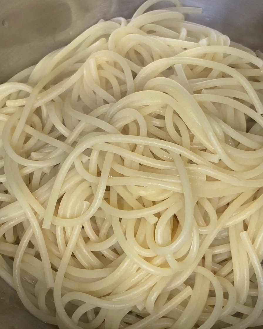 茹で上がったパスタにオリーブオイルを回しかけてボウルで和えている様子。