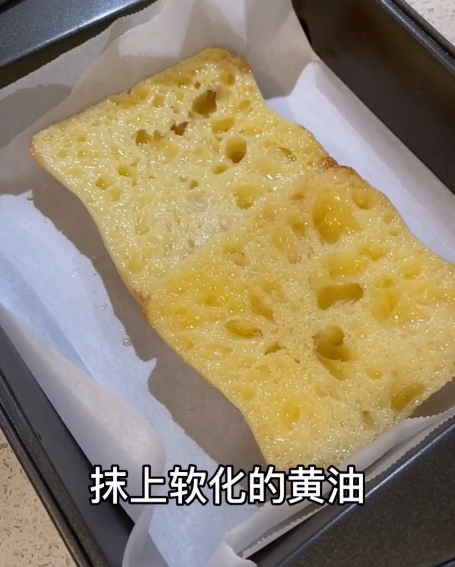 天板に並べたパンに柔らかいバターを丁寧に塗っている様子。