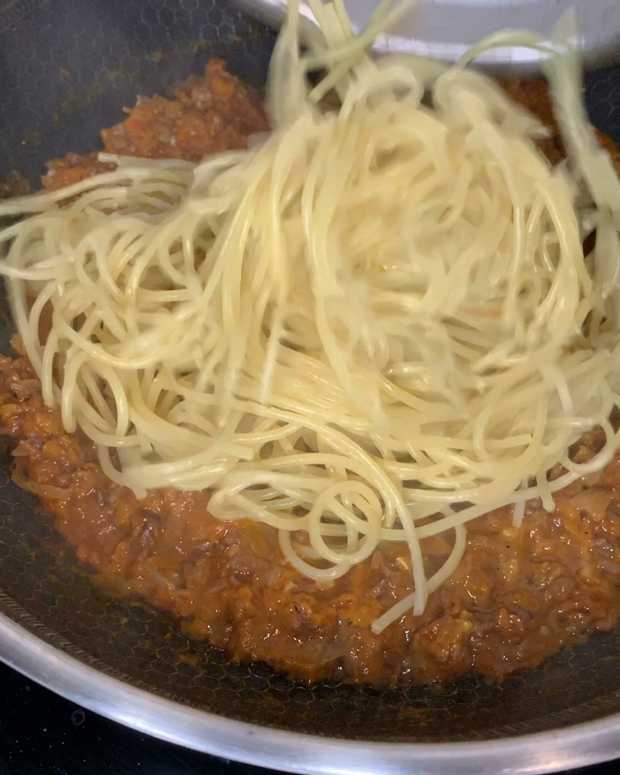 茹でた麺を濃厚なミートソースの中に入れて混ぜ合わせている様子。